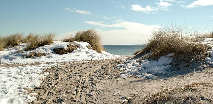 Stil ned til stranden på en smuk vinterdag Nedgang til stranden mellem klitter med sol og sne