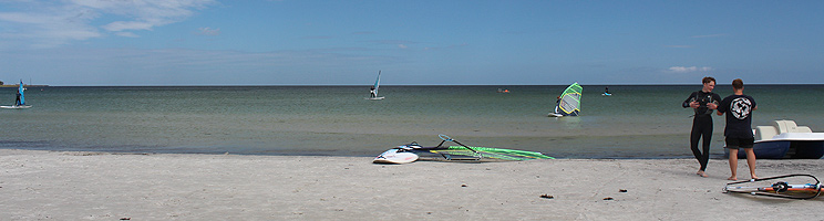 Surfer am breiten Sandstrand mit seichtem und klarem Badewasser in Balka Surfer am breiten Sandstrand mit seichtem und klarem Badewasser in Balka