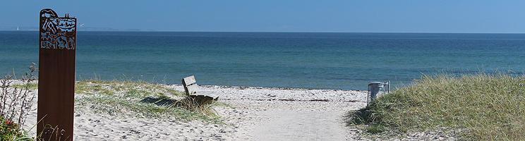 Kunstværk og bænk ved Saksilds dejlige sandstrand med lavt, klart vand Kunstværk og bænk ved Saksilds dejlige sandstrand med lavt, klart vand