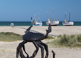 Das Wahrzeichen von Slettestrand, eine eiserne Krabbe, vor den Fischerbooten auf dem Strand Das Wahrzeichen von Slettestrand, eine eiserne Krabbe, vor den Fischerbooten auf dem Strand
