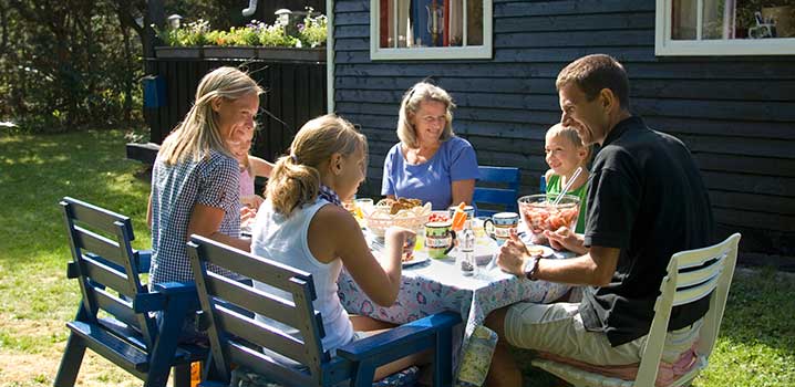 Familie på fire personer er samlet til spisning omkring et bord udenfor deres sommerhus