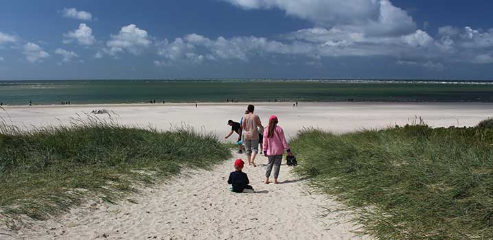 Familie løber på stranden med vand og blå himmel i baggrunden