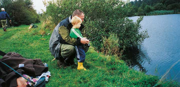 Far og søn fisker i en fiskesø