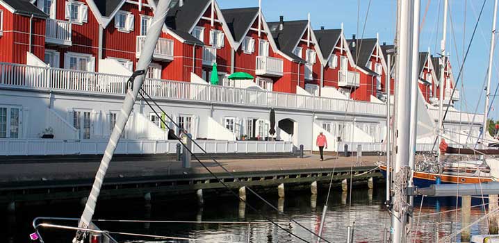Røde og hvite ferieleiligheter på rad og rekke ut mot lystbåthavn med båter.